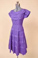 Load image into Gallery viewer, Vintage 50's midi length purple day dress is shown from the side. This dress has a boat neckline with cap sleeves.