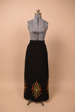 Load image into Gallery viewer, Vintage 60&#39;s black cotton maxi skirt is shown from the front. This skirt has boho colorful patterns embroidered at the bottom hem. 
