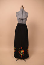 Load image into Gallery viewer, Vintage 60's black cotton maxi skirt is shown from the front. This skirt has boho colorful patterns embroidered at the bottom hem.