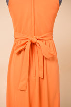 Load image into Gallery viewer, Vintage bright orange seventies poly maxi dress is shown from the back. This dress has a bow accent at the back of the waist. 
