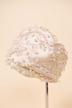 Load image into Gallery viewer, Vintage 1950s cream couture satin turban by Christian Dior is shown from the side. This silky turban is covered in tear shaped crystal and pearl beads. 
