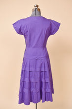 Load image into Gallery viewer, Vintage fifties grape purple cotton day dress is shown from the back. This dress ruffled details on the skirt.
