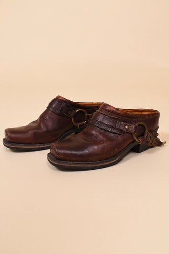 Secondhand dark brown leather harness mules by Frye are shown from the side. These leather boot mules have a low chunky heel. 