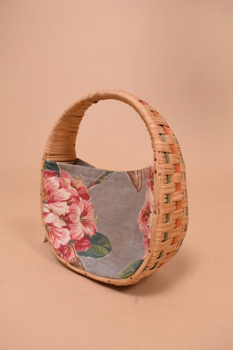 Vintage 1970's fabric and woven handbag is shown from the side. This handbag has a floral printed grey and pink fabric.