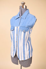 Load image into Gallery viewer, Vintage white and blue denim sleeveless button down is shown from the side. This light wash denim top has a pointed collar. 
