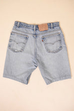 Load image into Gallery viewer, Vintage 1980s orange tab light wash denim long shorts are shown from the back. 
