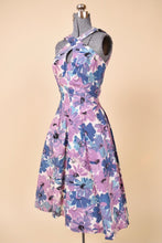 Load image into Gallery viewer, Vintage 50s purple and blue flower print tea dress is shown from the side. This classic fifties dress has a full pleated skirt. 
