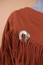 Load image into Gallery viewer, Vintage western aesthetic burnt orange fringe long sleeve top is shown in close up. This cotton shirt has a silver coin accent with a star design.
