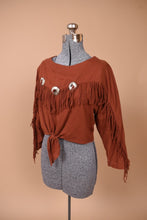 Load image into Gallery viewer, Vintage rust Western style tie waist cropped long sleeve top is shown from the side. This cowboy aesthetic top has silver accents on the chest. 
