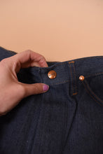 Load image into Gallery viewer, A hand holds up the front center button. The button is gold.