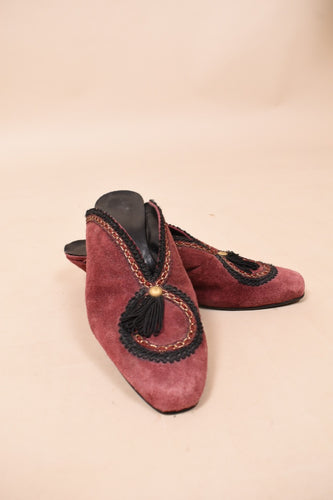Red suede mules are shown from the front. These mules have black embroidery with gold details.