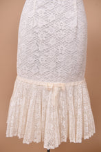 Load image into Gallery viewer, Vintage 1960s white floral lace mermaid dress is shown in close up. This dress has a cream ribbon accent above a pleated sheer lace skirt.
