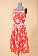 Load image into Gallery viewer, 1970s red and white floral dress is shown from the side. This dress has a tie at the waist.
