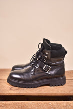 Load image into Gallery viewer, Black vintage combat boots by All Saints are shown from the side. The boots have a large silver buckle.
