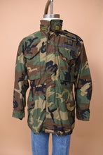 Load image into Gallery viewer, The jacket faces forward on the mannequin. The piece is zippered up the neck. There are two front pockets.
