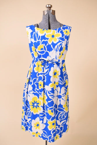 Vintage 1960's blue and yellow bright floral print sleeveless midi dress is shown from the front. This dress has an empire waist with a bow. 