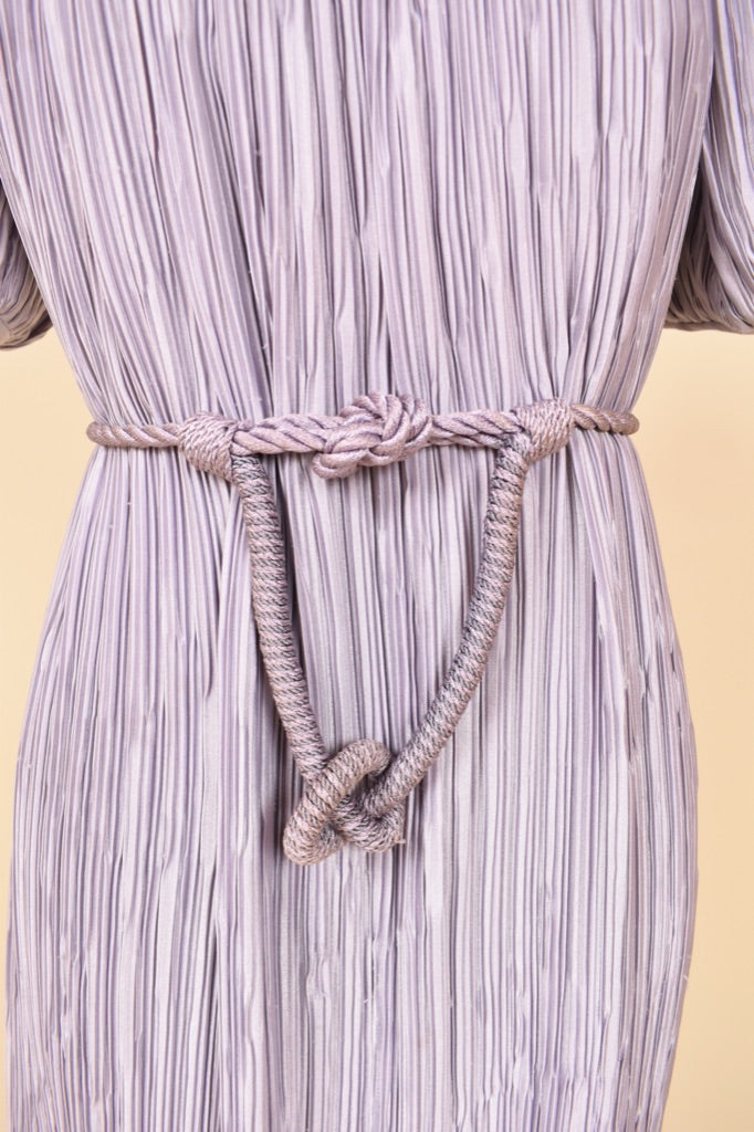Vintage eighties designer midi length pleated dress is shown in close up. This dress cinches with a rope belt at the waist. 