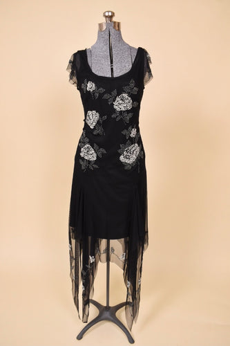 Vintage 1990's black sheer beaded handkerchief dress by Sue Wong is shown from the front. This dress has silver beaded roses on the front. 