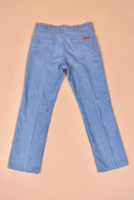 Load image into Gallery viewer, Vintage 70s light wash denim jeans are shown from the back. These flare jeans have a pleat down the leg. 
