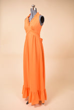 Load image into Gallery viewer, Vintage 70s halter neck ruffle trim orange polyester gown is shown from the side. This dress has a bottom ruffle tier. 
