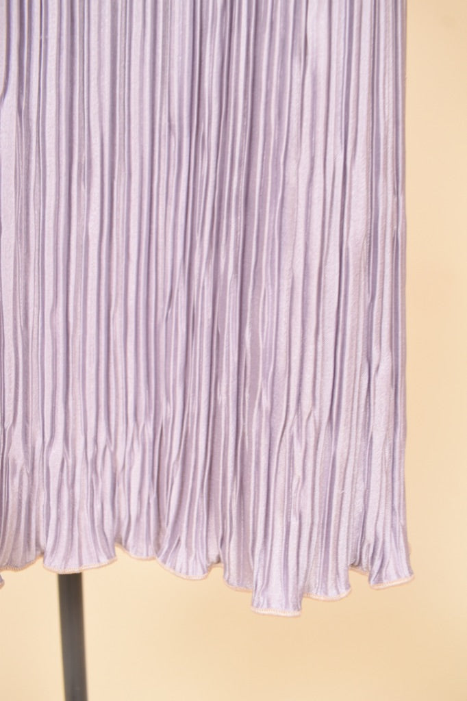 Lavender purple pleated designer midi dress is shown in close up. 