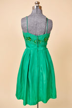 Load image into Gallery viewer, Vintage emerald green acetate sixties mini cocktail dress is shown from the back. This dress is tailored at the waist with a full skirt. 
