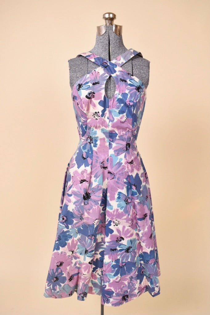 Vintage 1950's cross front purple and blue floral print day dress is shown from the front. This dress is sleeveless with a keyhole neckline. 