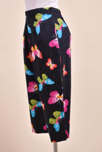 Load image into Gallery viewer, Vintage black Y2K capri pants are shown from the side. These black capri pants have rainbow butterflies. 
