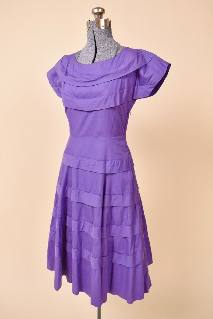 Vintage 50's midi length purple day dress is shown from the side. This dress has a boat neckline with cap sleeves. 