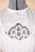 Load image into Gallery viewer, Vintage eighties antique inspired white lace bib dress is shown in close up. This dress has a delicate floral lace at the neck. 

