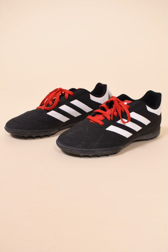 Vintage black and white Adidas soccer cleats are shown from the side. These soccer cleats have red laces. 