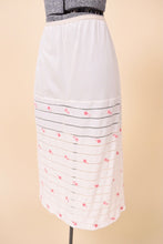 Load image into Gallery viewer, Vintage white embroidered midi length slip skirt is shown from the side. This skirt has sheer horizontal stripe panels. 
