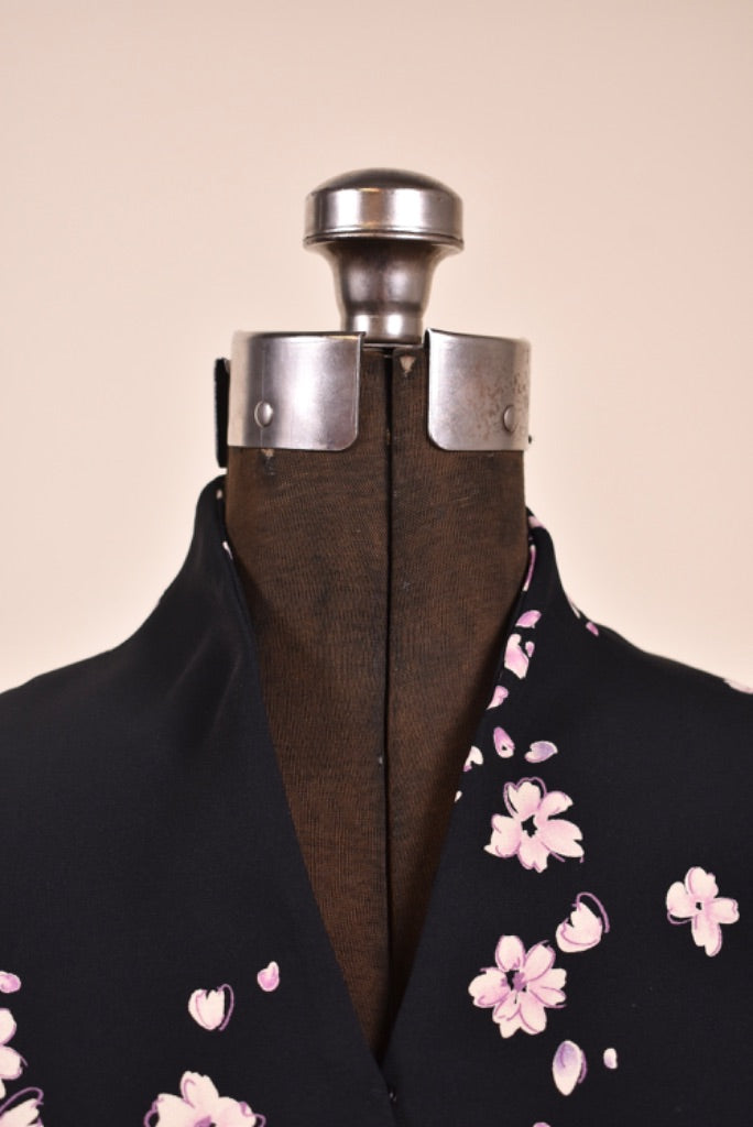 Vintage black and pink floral print dress is shown in close up. This dress has a raised collar with a v neckline. 
