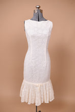 Load image into Gallery viewer, Vintage 1960s white lace mermaid dress is shown from the front. This dress has a drop waist with a pleated lace skirt.
