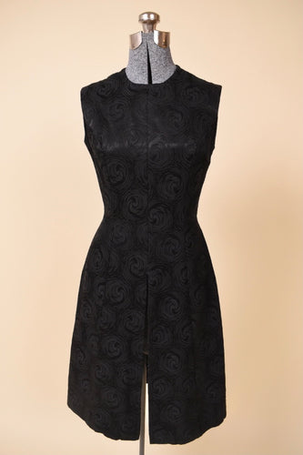 Vintage 1960's black silk jacquard tunic dress by Plymouth is shown from the front. This sleeveless rose print black dress has a high slit up the front of the skirt. 