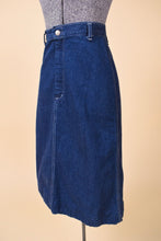 Load image into Gallery viewer, Vintage 1970&#39;s dark wash navy blue denim midi length skirt is shown form the side. This skirt has white stitching. 
