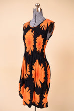 Load image into Gallery viewer, Vintage black and orange sunflower print midi day dress is shown from the side. This dress is black with an orange graphic flower print.
