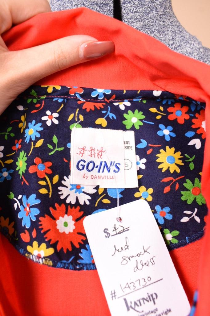 Vintage sixties red smock dress shown in close up. This dress has a tag which reads Go Ins.