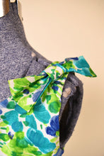 Load image into Gallery viewer, Vintage 60s white, blue, and green floral print dress is shown in close up. This dress has a bow at the shoulder. 
