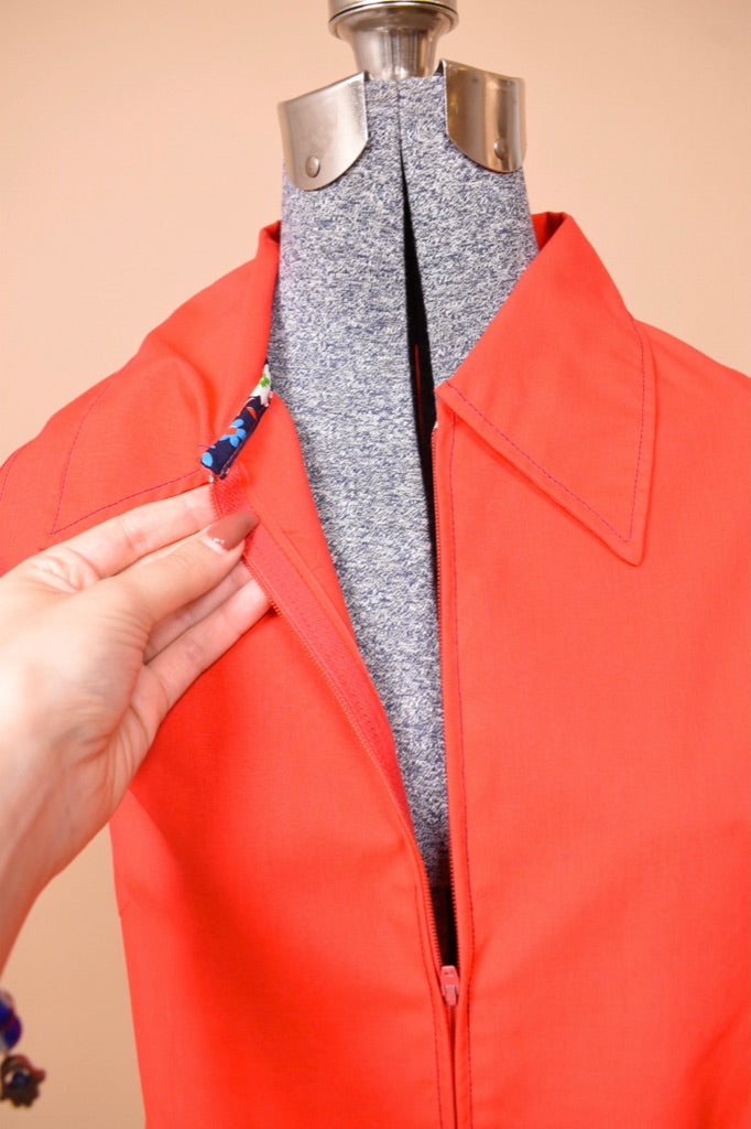 Red seventies zip up house dress shown in close up. The dress is held open to show the navy floral trim.