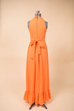 Load image into Gallery viewer, Vintage seventies ruffled orange polyester maxi dress is shown from the back. This dress has a belt that ties in a bow at the waist. 
