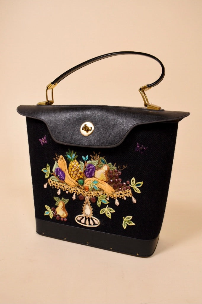 Vintage 1960's Enid Collins black leather and canvas bucket bag is shown from the front. This bag has a fruit platter embroidered on the front with gems.