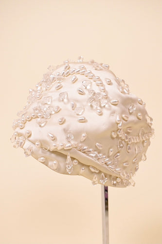 Vintage 1950s cream couture satin turban by Christian Dior is shown from the side. This silky turban is covered in tear shaped crystal and pearl beads. 