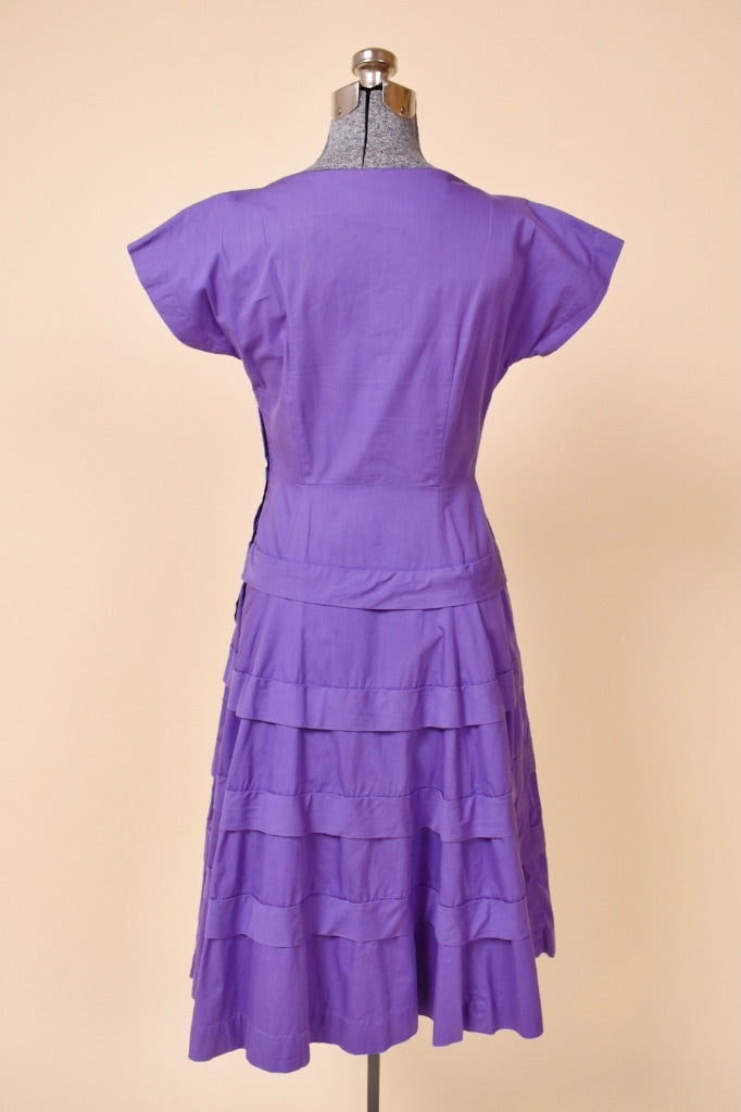Vintage fifties grape purple cotton day dress is shown from the back. This dress ruffled details on the skirt. 