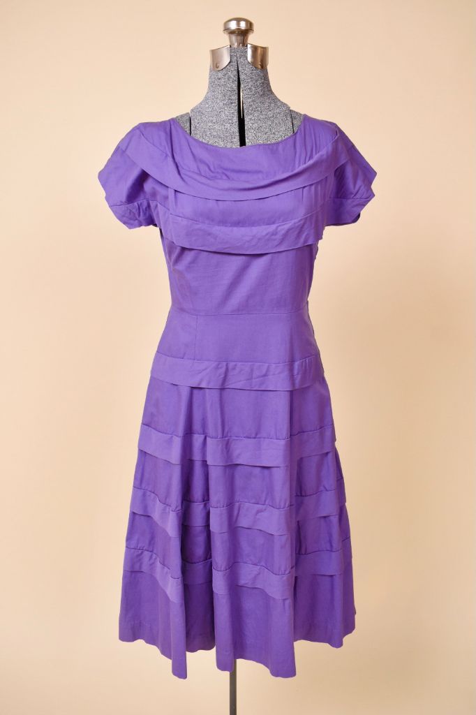 Vintage 1950's purple cotton dress is shown from the front. This dress has draped ruffles at the neckline and skirt. 