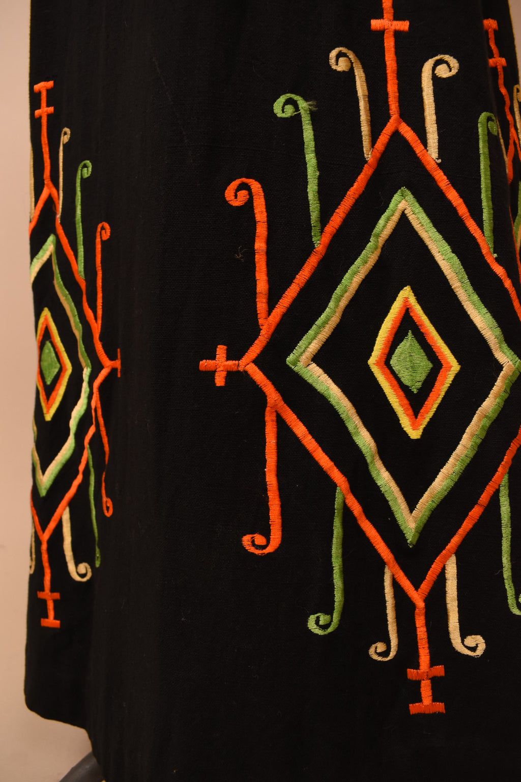 Vintage black cotton sixties maxi skirt is shown in close up. This skirt has shiny embroidered diamond designs at the bottom hem in orange, green, and yellow tones.