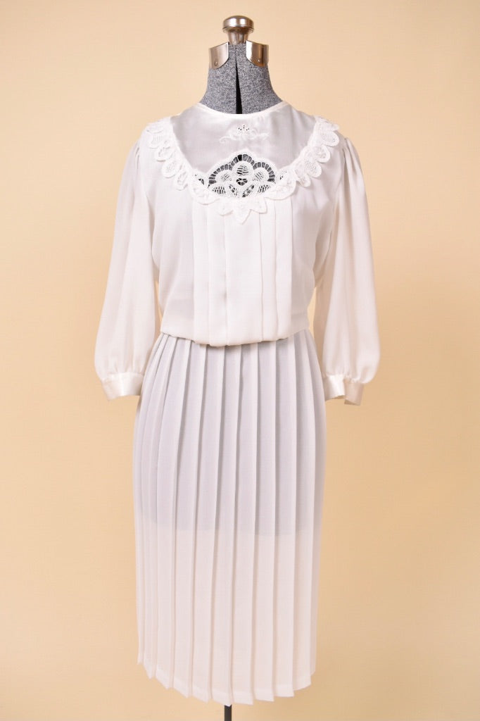 Vintage 1980's white pleated midi dress is shown from the front. This sheer mutton sleeve dress has a lace bib detail.