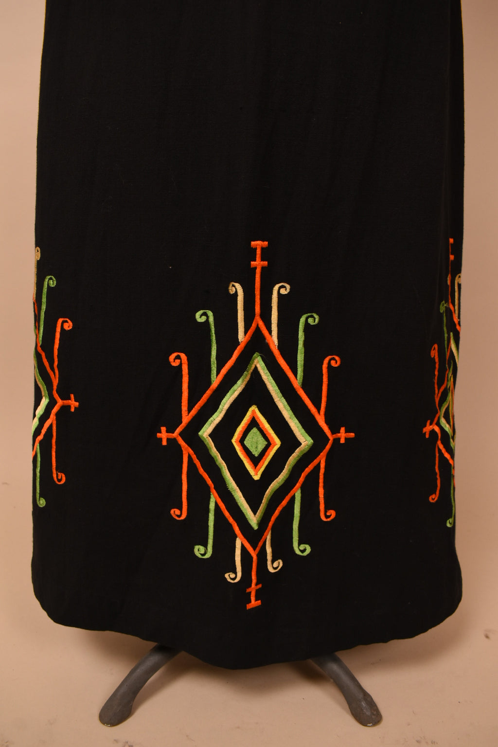 Vintage 1960s black cotton maxi skirt is shown in close up. This skirt has an artsy red, green, and yellow diamond shaped design at the bottom hem.