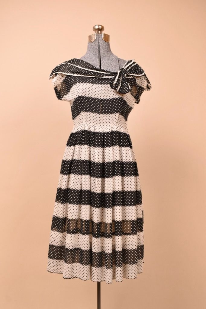 Vintage 1950's black and white striped polka dot tea dress is shown from the front. This dress has an asymmetrical neckline with a bow.