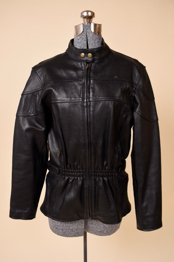 Vintage black leather cinched waist moto jacket is shown from the front. This jacket has a patchwork detail on the bust. 